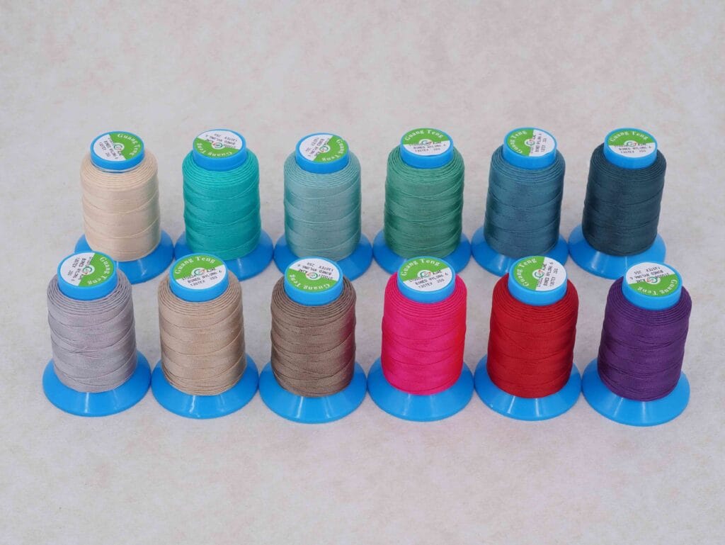 Row of pastel colored thread spools on blue stands arranged in a gradient from beige to navy in a neat row
