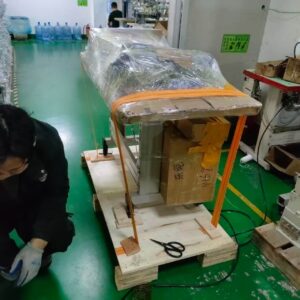 Industrial workspace with a partially wrapped machine secured on a wooden pallet with orange straps in a factory setting.