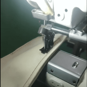 Industrial sewing machine sewing a beige fabric along a stitched seam, with the needle and presser foot in view.